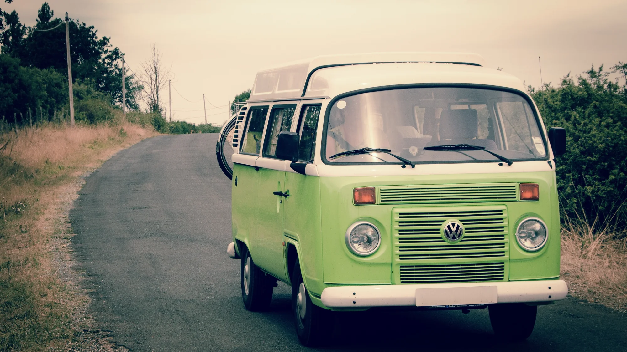 A Volkswagen Type 2 bay-window bus parked on a dirt track under an evening sky.