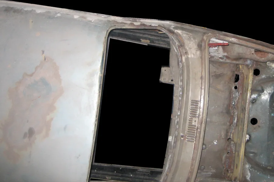 A gloved hand block-sanding a bare metal Volkswagen bus body panel.
